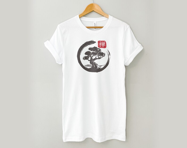 Puede incluir: Camiseta blanca con una ilustraci&oacute;n en blanco y negro de un &aacute;rbol en un c&iacute;rculo con la palabra japonesa "Zen" en rojo.