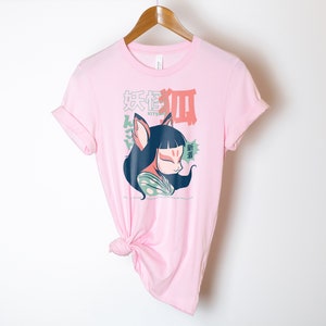 Peut inclure: T-shirt rose avec un graphique d'un renard de dessin anim&eacute; avec un masque kitsune, portant un kimono vert et blanc. Le texte "Kitsune" et des caract&egrave;res japonais sont imprim&eacute;s sur le t-shirt.