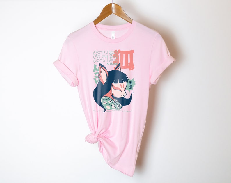 Peut inclure: T-shirt rose avec un graphique d'un renard de dessin anim&eacute; avec un masque kitsune, portant un kimono vert et blanc. Le texte "Kitsune" et des caract&egrave;res japonais sont imprim&eacute;s sur le t-shirt.