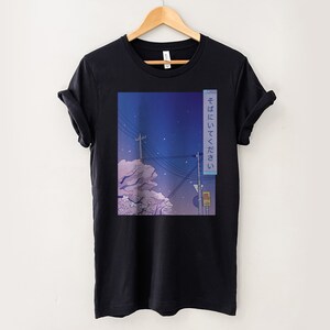 May include: Black t-shirt featuring a graphic print of a cityscape at night with a pink cherry blossom tree and the Japanese text "そばにいってほしい" which translates to "I want to be by your side".