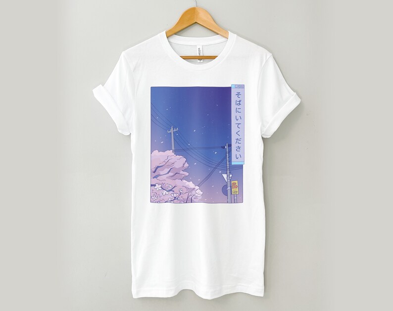 May include: White t-shirt featuring a graphic print of a cityscape at night with cherry blossoms and the Japanese text "そこにいてください" which translates to "Stay there".
