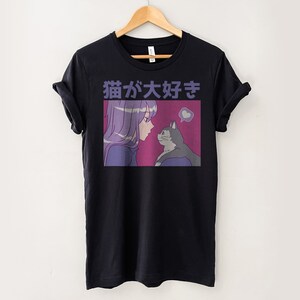 Puede incluir: Camiseta negra con un estampado gr&aacute;fico de una chica con el pelo morado mirando a un gato. El texto "猫が好き" est&aacute; impreso en la camiseta.