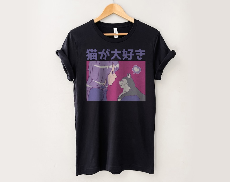 Puede incluir: Camiseta negra con un estampado gr&aacute;fico de una chica con el pelo morado mirando a un gato. El texto "猫が好き" est&aacute; impreso en la camiseta.