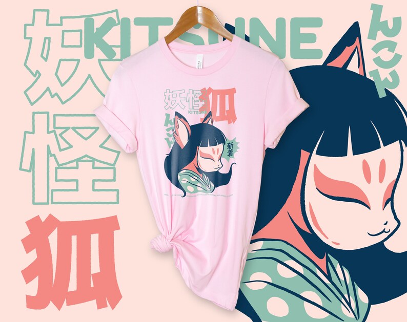 Peut inclure: T-shirt rose avec un motif repr&eacute;sentant une femme portant un masque de renard et le texte "KITSUNE" en caract&egrave;res japonais. Le texte "KITSUNE" est en vert et le texte japonais est en rouge et bleu.