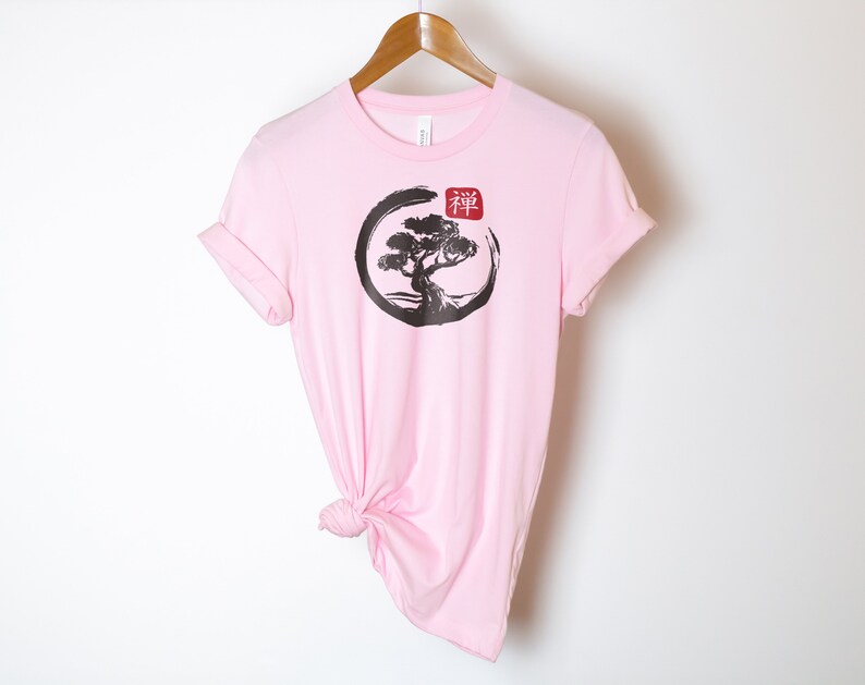 Puede incluir: Camiseta rosa con un gr&aacute;fico en blanco y negro de un &aacute;rbol en un c&iacute;rculo con la palabra japonesa "Zen" en rojo.