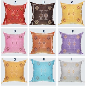 May include: Nine square throw pillows in various colors, each with a geometric design. Colors include red, brown, yellow, pink, orange, purple, light blue, and gray. Each pillow has a tassel on each corner.