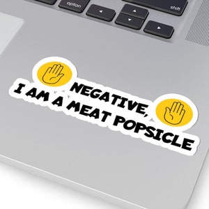 May include: A white sticker with black text that reads "NEGATIVE, I AM A MEAT POPSICLE". The sticker has two yellow hand icons with a black outline.