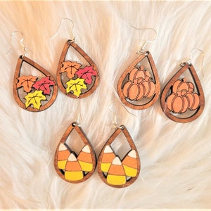 May include: A set of six wooden teardrop earrings with various fall-themed designs. The earrings feature images of autumn leaves, pumpkins, and candy corn.