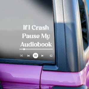 May include: A white vinyl decal on a vehicle window with the text "If I Crash Pause My Audiobook" and a media player graphic. The vehicle is a pink SUV, with a black tire visible.