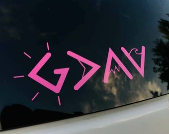 May include: Pink vinyl decal with the word "GOD" written in stylized letters. The letters are formed by geometric shapes, including a sunburst, an arrow, a mountain, and a wave.