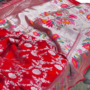 Puede incluir: Un textil rojo vibrante con intrincados patrones florales plateados y bordes. La tela presenta un dise&ntilde;o detallado de flores y hojas blancas, con un borde plateado adornado con motivos florales coloridos. La est&eacute;tica general es rica y ornamentada.