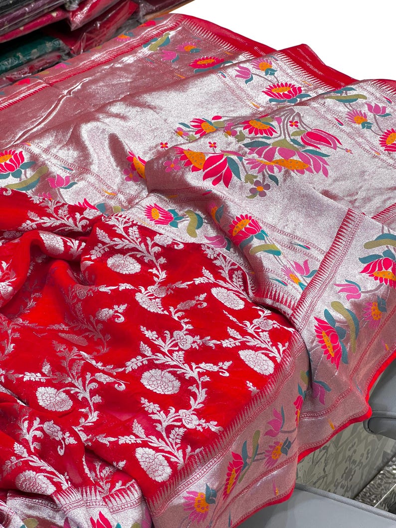 Puede incluir: Un textil rojo vibrante con intrincados patrones florales plateados y bordes. La tela presenta un dise&ntilde;o detallado de flores y hojas blancas, con un borde plateado adornado con motivos florales coloridos. La est&eacute;tica general es rica y ornamentada.