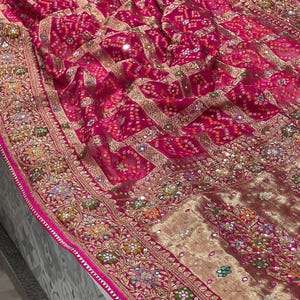 Puede incluir: Un sari rosa y dorado con bordados intrincados y lentejuelas. El sari tiene un borde floral y un patrón geométrico en el centro.