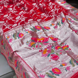 Puede incluir: Un tejido rojo vibrante con intrincados dise&ntilde;os florales. La tela presenta un borde plateado adornado con dise&ntilde;os florales coloridos en rosa, amarillo y verde. El dise&ntilde;o general es una mezcla de estilos tradicionales y contempor&aacute;neos.