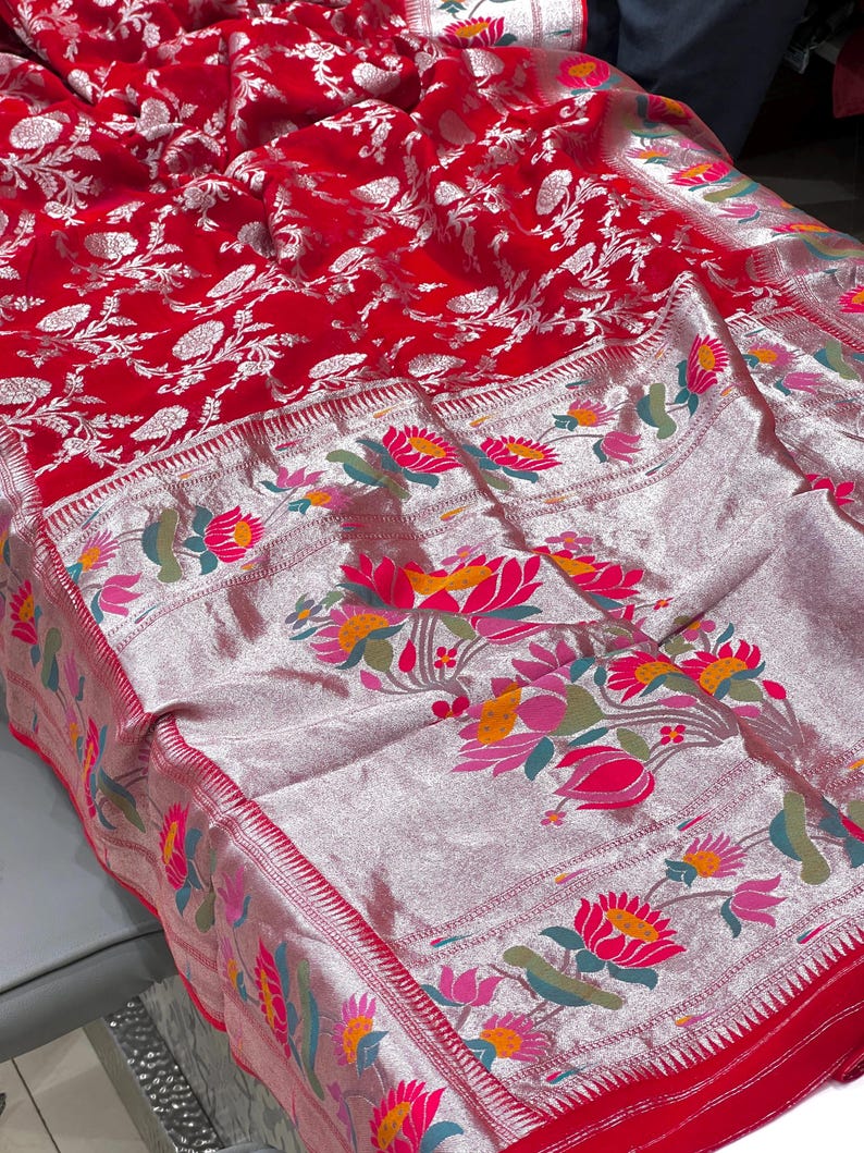 Puede incluir: Un tejido rojo vibrante con intrincados dise&ntilde;os florales. La tela presenta un borde plateado adornado con dise&ntilde;os florales coloridos en rosa, amarillo y verde. El dise&ntilde;o general es una mezcla de estilos tradicionales y contempor&aacute;neos.