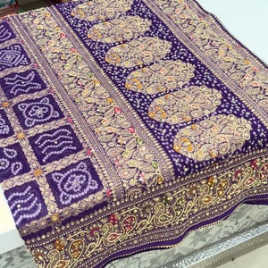 Pu&ograve; includere: Un tessuto viola dettagliato con motivi intricati. Il design presenta motivi floreali e geometrici ripetuti in tonalit&agrave; oro, beige e altri colori. Il bordo presenta un motivo a paisley.
