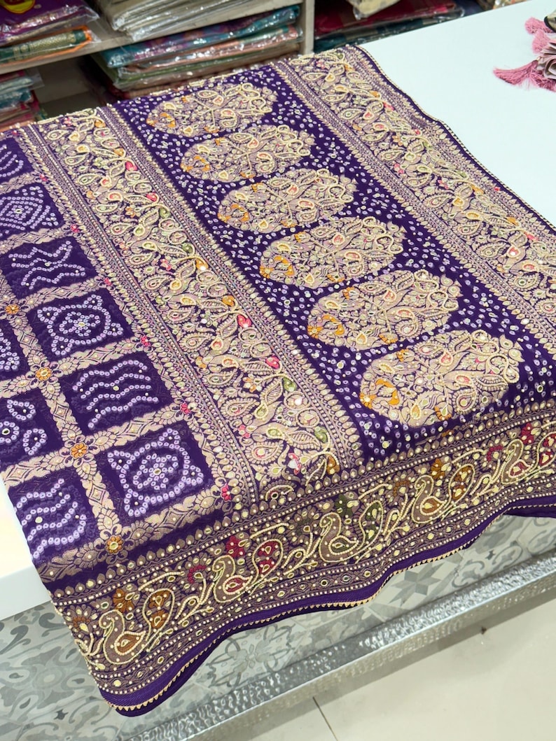 Pu&ograve; includere: Un tessuto viola dettagliato con motivi intricati. Il design presenta motivi floreali e geometrici ripetuti in tonalit&agrave; oro, beige e altri colori. Il bordo presenta un motivo a paisley.