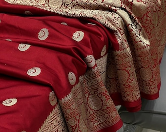 May include: A red silk saree with a gold border and intricate floral patterns. The saree has a traditional Indian design and is perfect for special occasions.