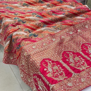 May include: A vibrant textile featuring a rich tapestry of colors, including red, orange, and pink. The fabric showcases intricate embroidery and embellishments, with floral and geometric patterns. The design includes a detailed border with ornate detailing.