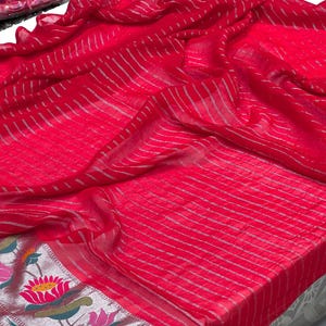 Puede incluir: Una tela roja vibrante con rayas plateadas y un borde floral. La tela est&aacute; drapeada, mostrando su textura y dise&ntilde;o. El borde presenta flores de loto y hojas coloridas.