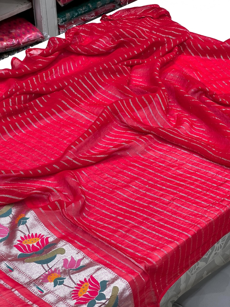 Puede incluir: Una tela roja vibrante con rayas plateadas y un borde floral. La tela est&aacute; drapeada, mostrando su textura y dise&ntilde;o. El borde presenta flores de loto y hojas coloridas.