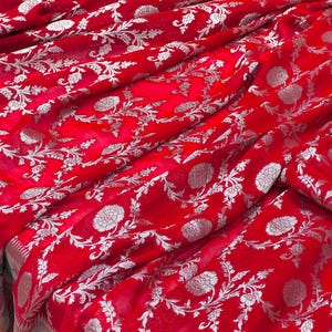Puede incluir: Tela roja brillante con un patr&oacute;n floral plateado. La tela est&aacute; drapeada, mostrando la textura y el dise&ntilde;o. El patr&oacute;n floral incluye flores y hojas detalladas.