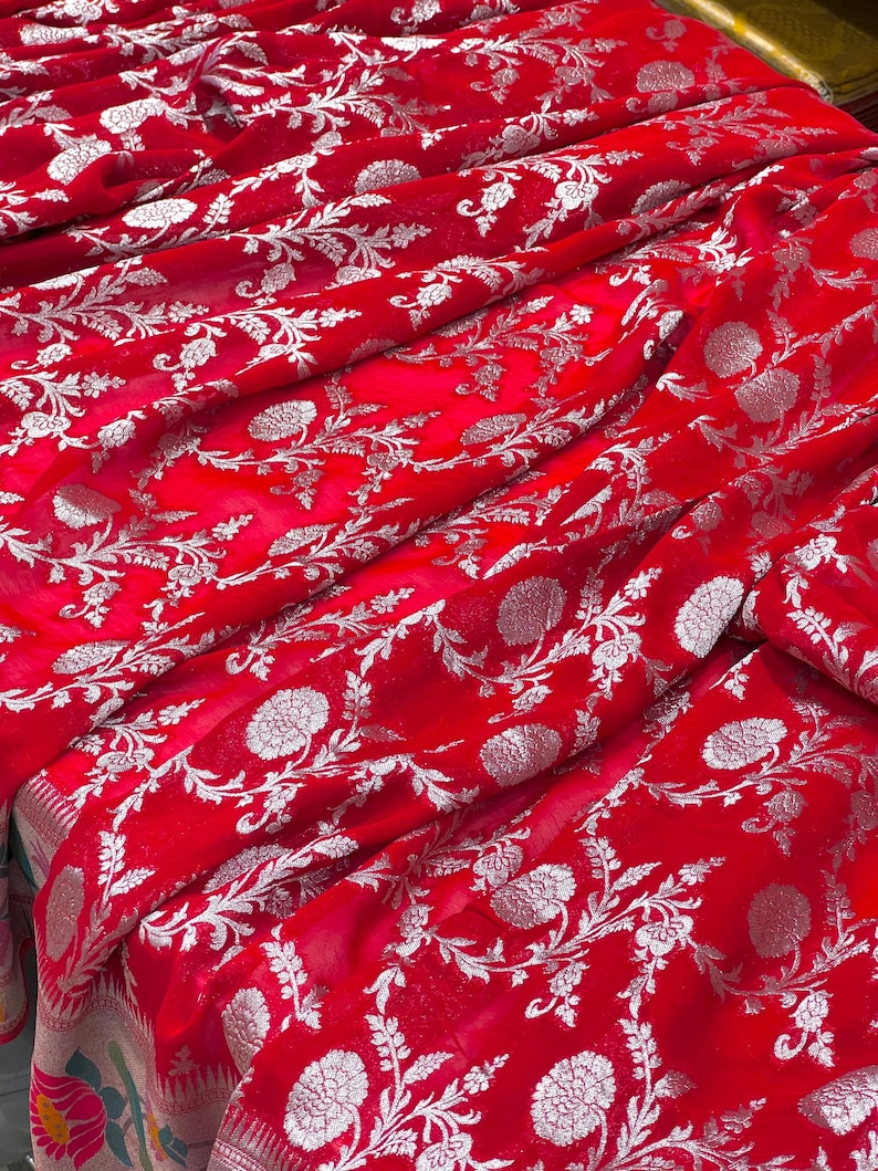 Puede incluir: Tela roja brillante con un patr&oacute;n floral plateado. La tela est&aacute; drapeada, mostrando la textura y el dise&ntilde;o. El patr&oacute;n floral incluye flores y hojas detalladas.
