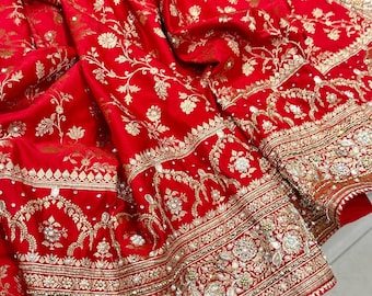 Puede incluir: Primer plano de un textil rojo vibrante con intrincado bordado floral dorado. La tela está ricamente detallada con patrones ornamentados y adornos, incluyendo delicadas cuentas a lo largo de los bordes. El diseño sugiere una prenda lujosa o una pieza decorativa.
