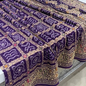 Pu&ograve; includere: Tessuto viola drappeggiato con un motivo dettagliato. Il tessuto presenta un motivo ripetuto di forme bianche e dorate, con un bordo dorato. Il tessuto &egrave; probabilmente utilizzato per abbigliamento o decorazioni per la casa.