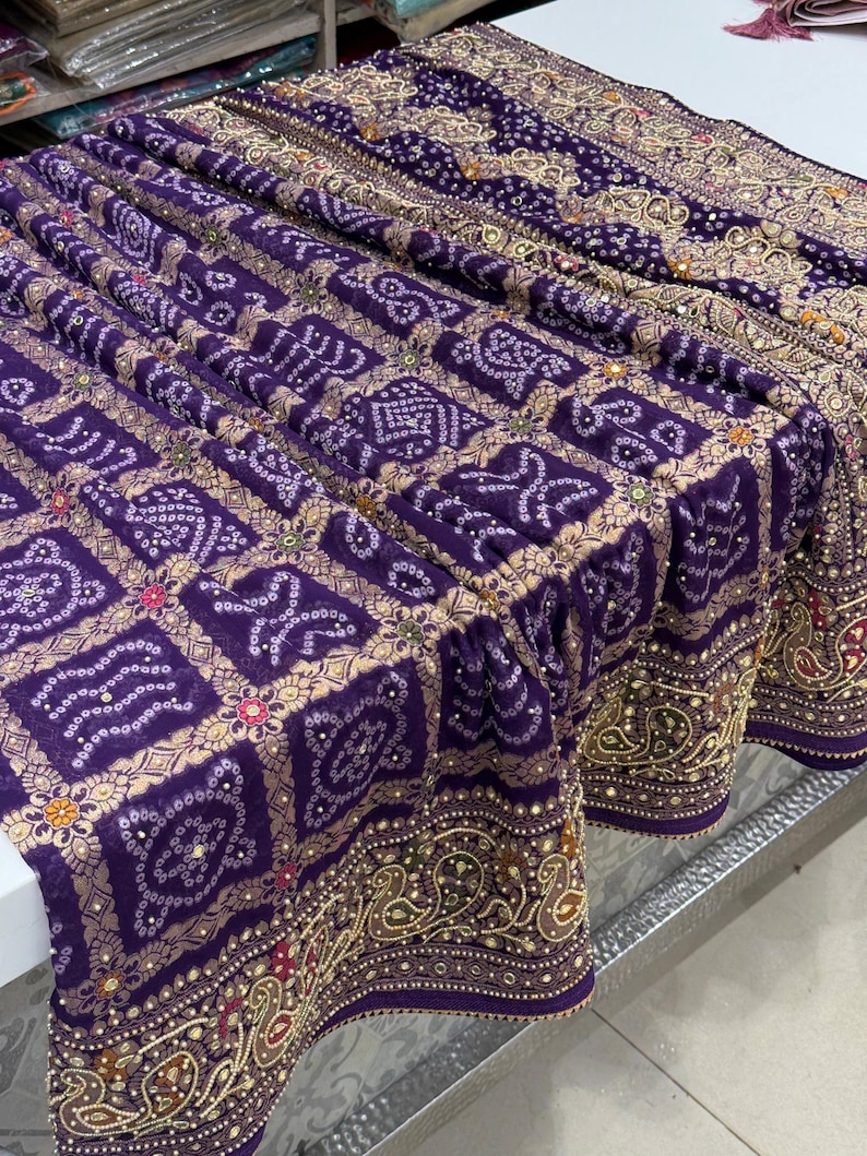 Pu&ograve; includere: Tessuto viola drappeggiato con un motivo dettagliato. Il tessuto presenta un motivo ripetuto di forme bianche e dorate, con un bordo dorato. Il tessuto &egrave; probabilmente utilizzato per abbigliamento o decorazioni per la casa.