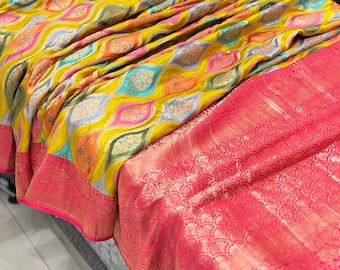 May include: A yellow, pink, and blue patterned silk saree with a pink border and a gold trim. The saree has a decorative fringe.