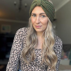 Pode incluir: Uma faixa de cabeça verde tricotada com um design de nó. A faixa de cabeça tem manchas de vermelho, laranja e amarelo. A pessoa na imagem está usando uma camisa de manga comprida com estampa de leopardo.