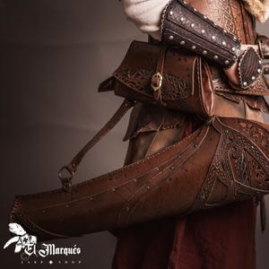 Puede incluir: Primer plano de un carcaj de cuero marrón con intrincados grabados, que contiene flechas con puntas negras. El carcaj forma parte de un conjunto de cuero más grande, que incluye protectores de brazos y un arco. Tema medieval o de fantasía.