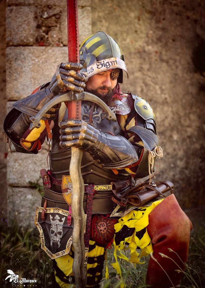 K&ouml;nnte beinhalten: Eine Person in mittelalterlicher R&uuml;stung und einem Helm mit gelbem und schwarzem Streifenmuster. Die Person h&auml;lt ein Schwert und hat ein Totenkopf- und Knochenkreuz-Emblem auf der Brust. Der Text "us Sigm" ist auf dem Helm sichtbar.