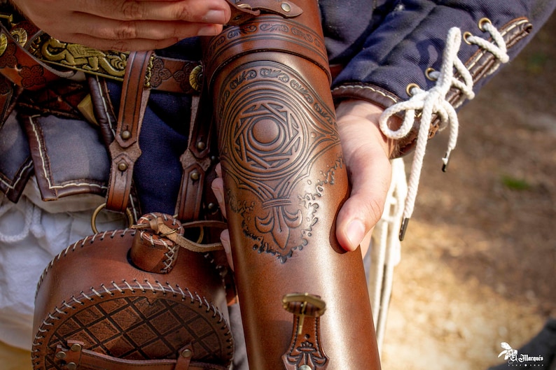 Peut inclure: Un carquois en cuir brun avec des motifs en relief complexes. Le carquois est dot&eacute; d'une sangle et d'une fermeture &agrave; boucle.
