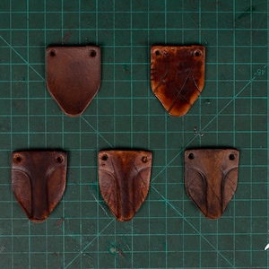 May include: Five brown leather patches with holes in the corners. The patches are on a green grid background.