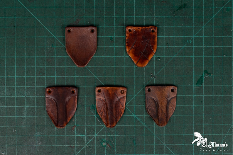 May include: Five brown leather patches with holes in the corners. The patches are on a green grid background.