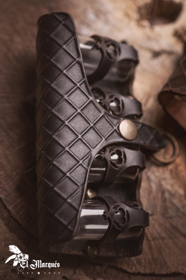 Peut inclure: Brassard en cuir noir avec un motif en losanges et des lani&egrave;res d&eacute;coratives. Le brassard a une fermeture &agrave; bouton en laiton et est con&ccedil;u pour la protection. C'est une pi&egrave;ce d'armure.
