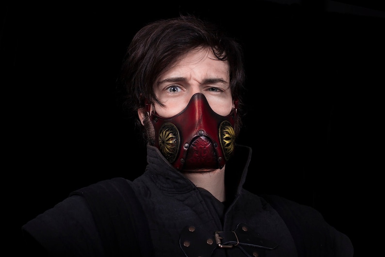 May include: A person wearing a red leather mask with gold accents and a black shirt.