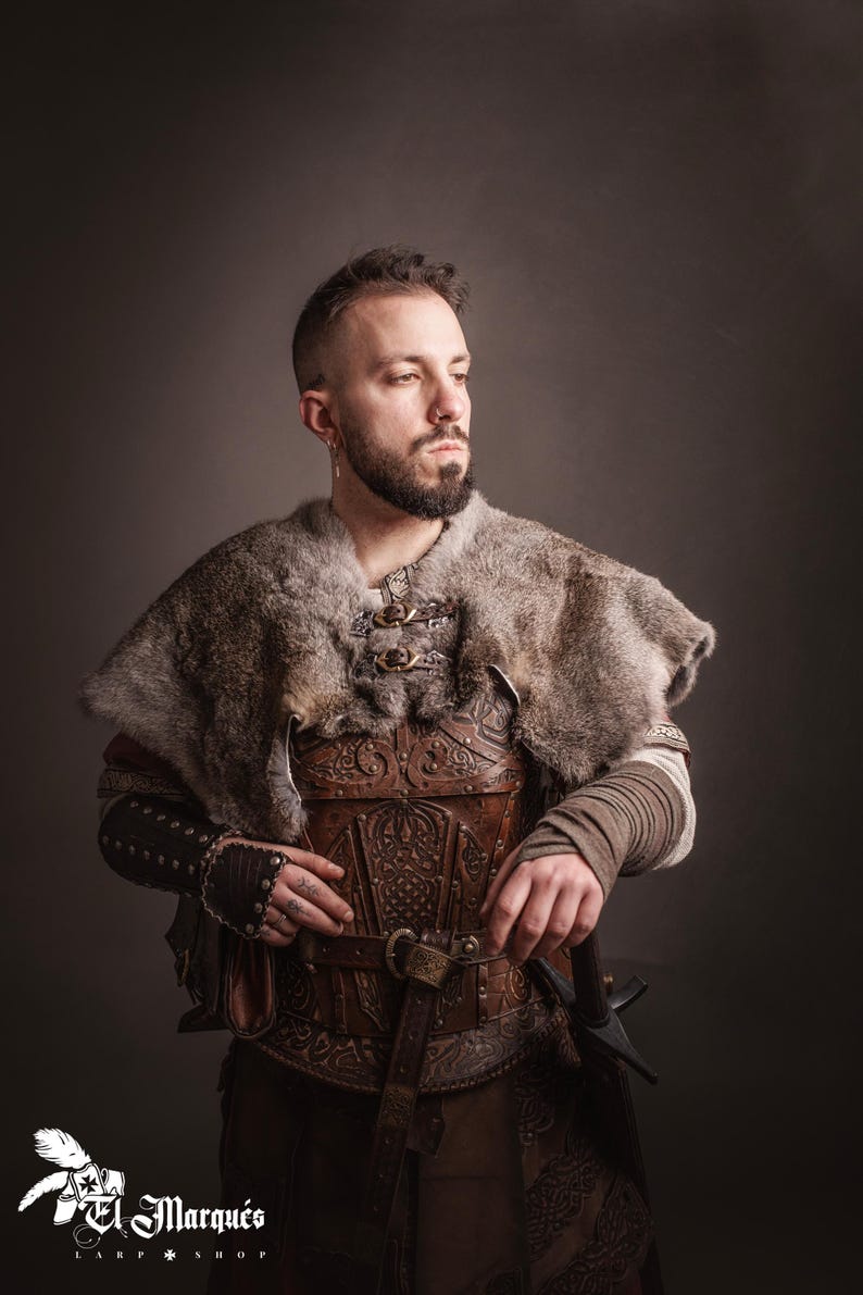 May include: A person wearing a brown leather armor with intricate carvings, a fur-lined cloak, and a sword. The armor is decorated with a belt and buckles. The person is standing against a gray background.