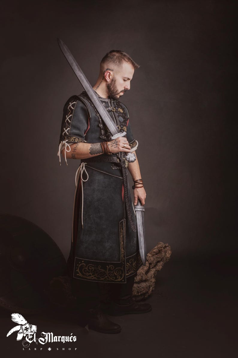 Peut inclure: Un costume m&eacute;di&eacute;val gris fonc&eacute; avec des d&eacute;tails dor&eacute;s, une longue &eacute;p&eacute;e et un poignard. Le costume pr&eacute;sente des coutures complexes et des d&eacute;tails en cuir. L'image est sur fond sombre, mettant en valeur les d&eacute;tails du costume et des armes.