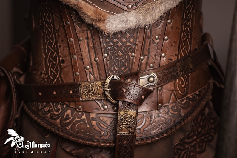 May include: A brown leather corset with intricate designs and a fur trim. The corset has a belt with a metal buckle and a decorative metal piece.