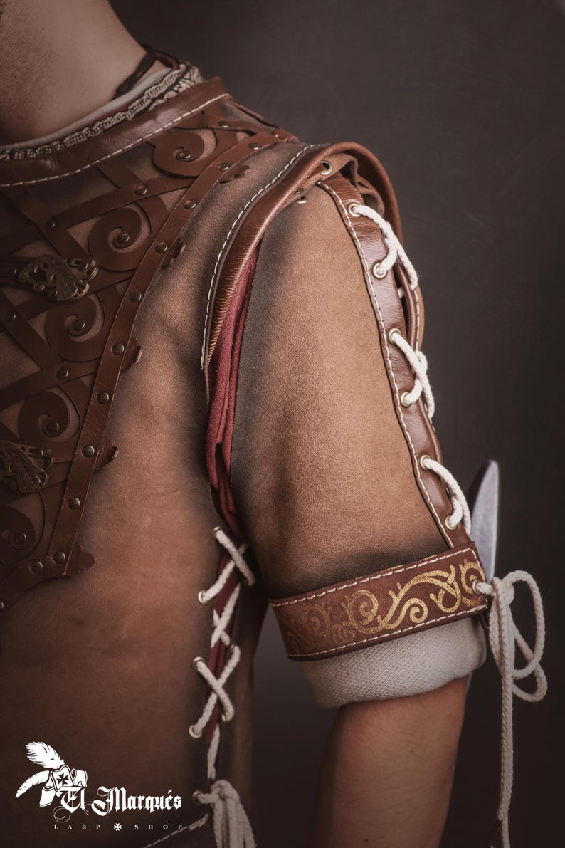 Peut inclure: Gros plan sur une armure en cuir marron avec des coutures d&eacute;coratives et des accents dor&eacute;s. L'&eacute;paule et le bras pr&eacute;sentent des motifs complexes et des d&eacute;tails de la&ccedil;age. L'armure est probablement destin&eacute;e au cosplay ou &agrave; la reconstitution historique.