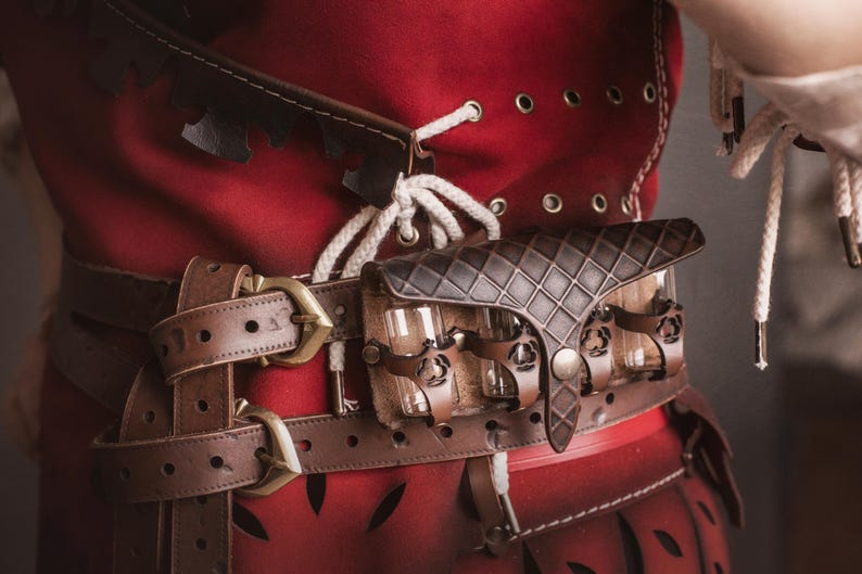 Peut inclure: Gros plan sur un v&ecirc;tement rouge avec une ceinture en cuir marron et une petite pochette. La ceinture a une boucle en laiton et la pochette a un motif en losanges. Le v&ecirc;tement a des &oelig;illets et des lacets blancs.