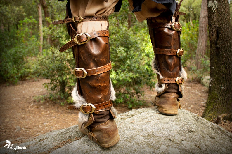 May include: Brown leather leg armor with gold buckles and fur trim. The armor is worn over brown boots.