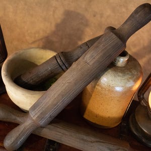 Könnte beinhalten: Ein Holz-Nudelholz mit rustikalem braunen Finish, ein Mörser und Stößel, ein Keramik-Krug und zwei antike Öllampen mit Glaskugeln.