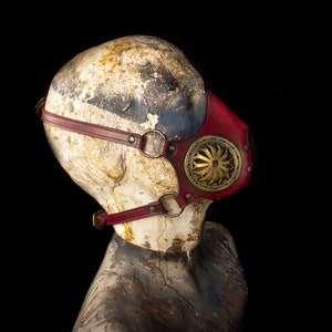 May include: A red leather steampunk-style mask with a gold metal gear design and adjustable straps.