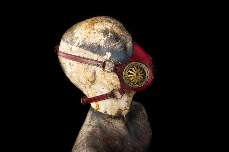 May include: A red leather steampunk-style mask with a gold metal gear design and adjustable straps.