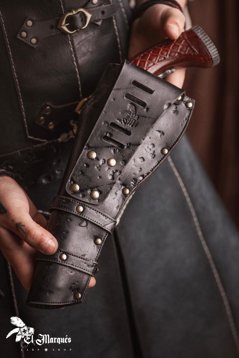Puede incluir: Una funda de cuero negra con un dise&ntilde;o decorativo y detalles met&aacute;licos. La funda est&aacute; dise&ntilde;ada para sostener una pistola.