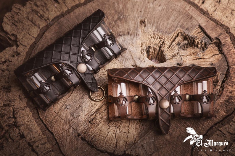 Peut inclure: Deux pochettes en cuir, une noire et une marron, avec un motif en losanges, sont pr&eacute;sent&eacute;es sur une surface en bois. Chaque pochette comporte des d&eacute;tails m&eacute;talliques d&eacute;coratifs et une fermeture &agrave; bouton. Les pochettes sont con&ccedil;ues pour contenir de petits flacons en verre.